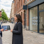 Deux personnes échangent devant une agence immobilière à Lille. L'homme présente des graphiques sur une tablette.